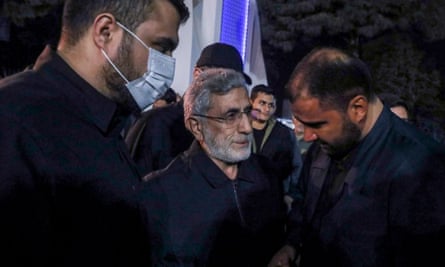 Man centre with grey beard next to two other men, one in a mask
