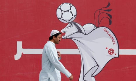A man passes a poster of the Qatar 2022 mascot La'eeb in Doha, Qatar.