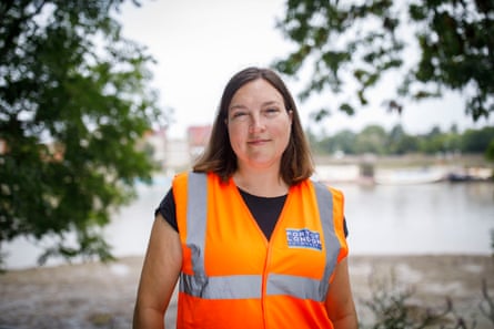 a woman in an orange hi-vis vest standing by the bank of the Thames