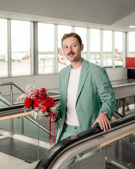 man in green suit carrying flowers arrives at the top of an escalator