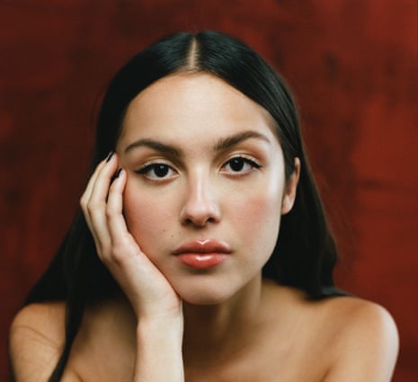 A portrait of Olivia Rodrigo against a dark red background