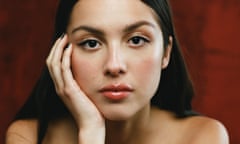 A portrait of Olivia Rodrigo against a dark red background