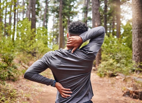 Unrecognizable mixed race hispanic male stretching before a run while experiencing some back and neck pain in a forest.