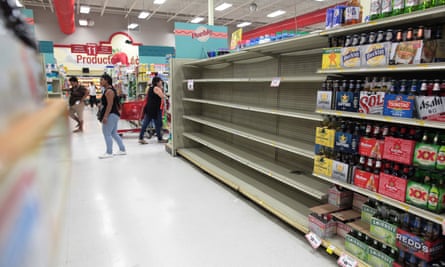 Customers in Puerto Rico walk near empty shelves that are normally filled with bottles of water. The governor has declared a price freeze on basic necessities.