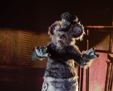 David Howard Thornton, in creature costume with large ears and sailor's hat, raises both paws in a dimly lit setting