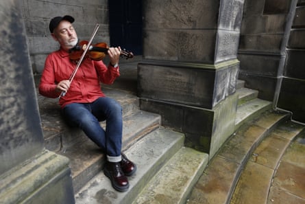 Aidan O’Rourke playing the fiddle on the steps of an old stone building