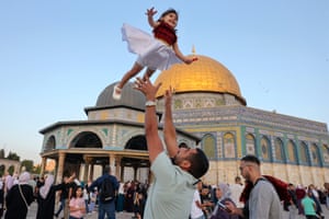 A man throws a child in the air outside a mosque with a golden dome