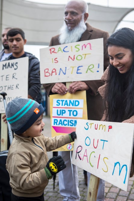 A group of people holding anti-racism banners including a childlooking at his own banner, which says 'Stump out racism' in colourful letters