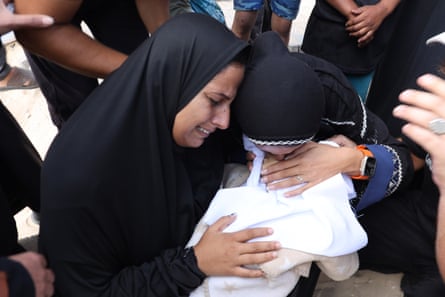 Women in black robes cry over a small bundle wrapped in white.