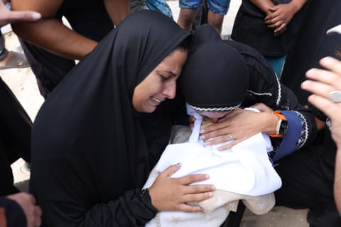 زنانی با ردای سیاه بر سر بقچهای کوچک که با پارچهای سفید پیچیده شده، گریه میکنند.