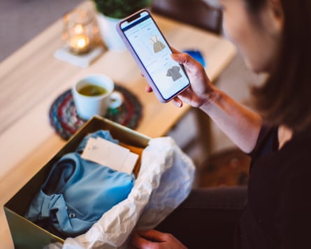 Young woman doing online shopping for clothes on smartphone with a delivered package from online shop putting in front of her.