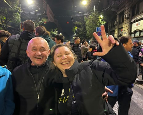 Stanislava laughs and raises a peace sign with a man beside her on a crowded night street
