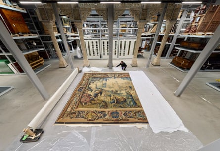 A museum worker helps to unroll an enormous decorative carpet in the middle of a museum work space