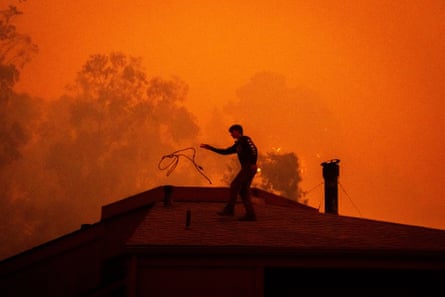 Silhouette of man on roof of house, with sky completely orange and smoky.