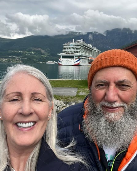 Elizabeth and Maged El-Nakla, family snapshot showing them in front of an expanse of water with large ship in background. Elizabeth has long silver-grey hair; Maged has a bushy grey beard and is wearing an orange woollen hat