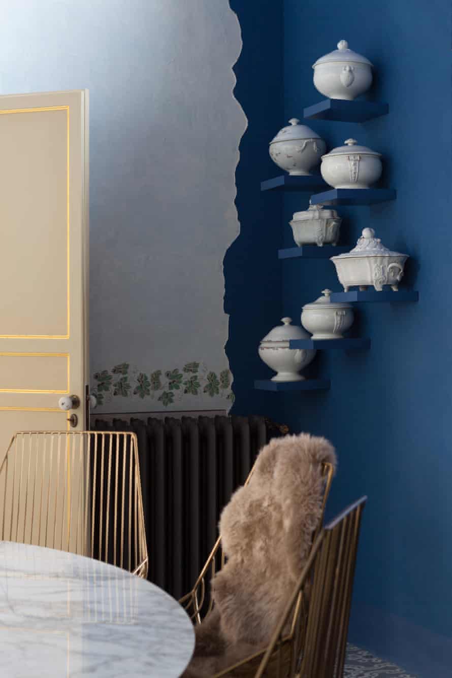 A blue painted wall with pots on small shelves running up the wall