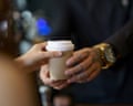 Barista serving coffee in takeaway paper disposable cup to customer in coffee shop