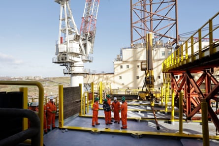 Kemi Badenoch stands in a group on an oil rig amid tall metal structures.