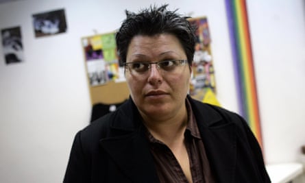Rauda Morcos, with short hair and glasses, in her office in 2007 with a few photos on the wall behind her and a vertical rainbow