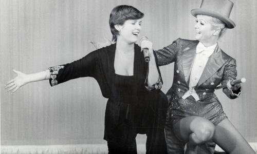 did carrie fisher smoke cigarettes sits between Mark Hamill and Harrison Ford, knees folded up against a table, holding a lit cigarette near an ashtray. Behind them, a wall lined with vending machines. Hamill Carrie Fisher's Demons Didn't Inhibit