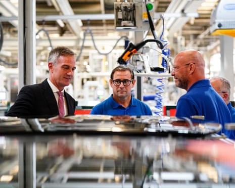 He wears suit and tie and talks to two workers
