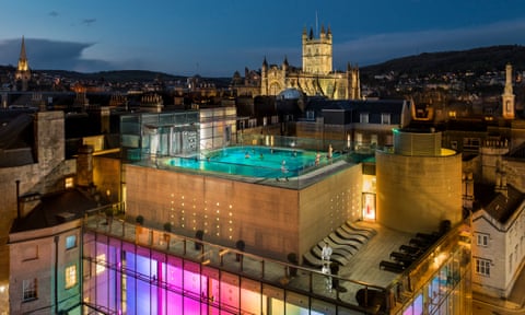 Aerial view of outdoor pool at Thermae Bath Spa by night, Bath, Somerset, with cathedral in background