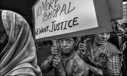 A grave-looking boy holds a placard reading 'no more Bhopal. We want justice'. Behind him a woman holds another placard