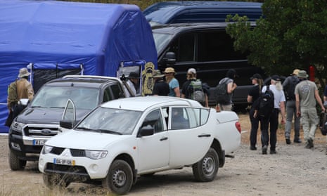 A group of people gathered among several vehicles and a large tent in an area of scrubland