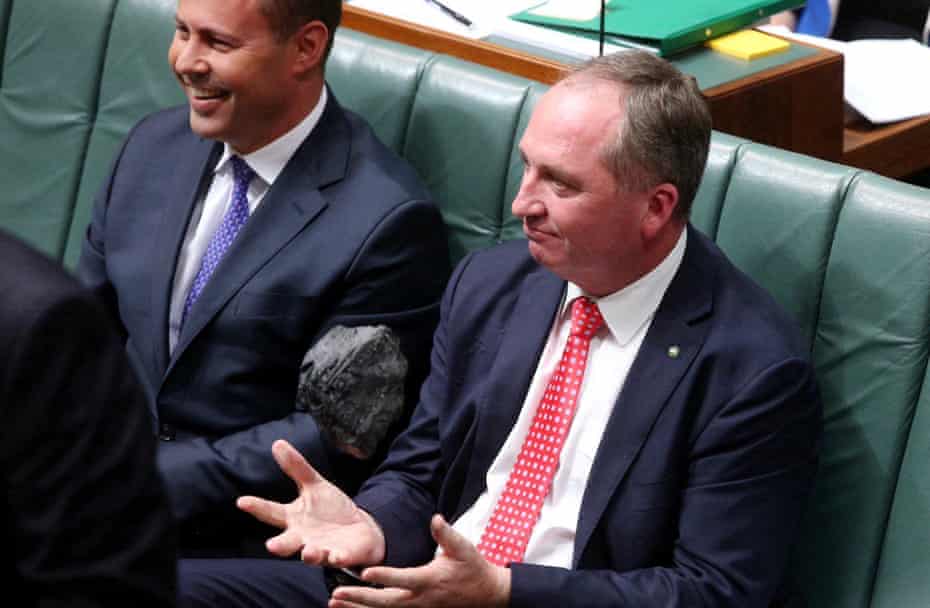Josh Frydenberg sitting next to Barnaby Joyce, who is tossing a piece of coal in parliament.