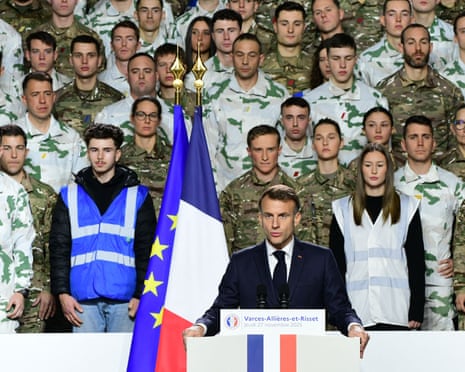 Emmanuel Macron talking at a podium with a French flag, people in military attire behind him.