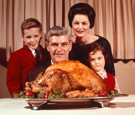A family in the 1960s stands together for a portrait with a roast turkey in the foreground.