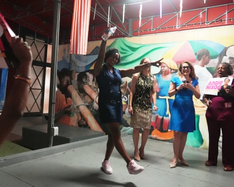 Angie Nixon smiles and raises a water bottle while dancing before a colourful mural at a campaign event