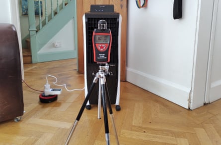 A living room is pictured with an air cooler in front of a digital thermometer