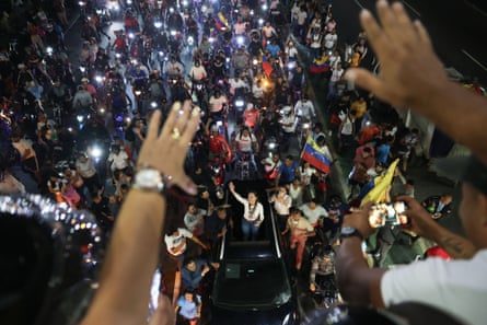 Maria Corina Machado waves from a car roof amid a large crowd of supporters at night