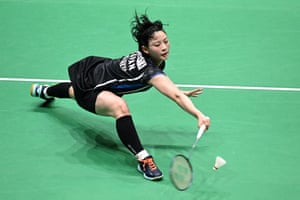 A Badminton player lunges dramatically with her racket to reach the shuttlecock on a Badminton court