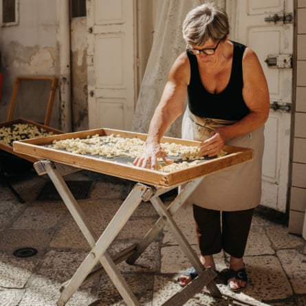 A woman stands at a table of pasta
