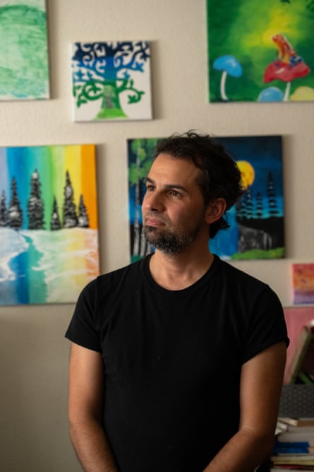 A man looking upward beyond the camera, as he stands in front of a wall covered with outdoorsy art.
