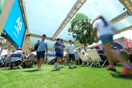 People walk across grass next to an Australian Open screen