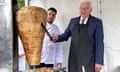 Frank-Walter Steinmeier in a suit with an apron over the top, cutting meat from a kebab, as Arif Kele?, in a white chef’s jacket, watches