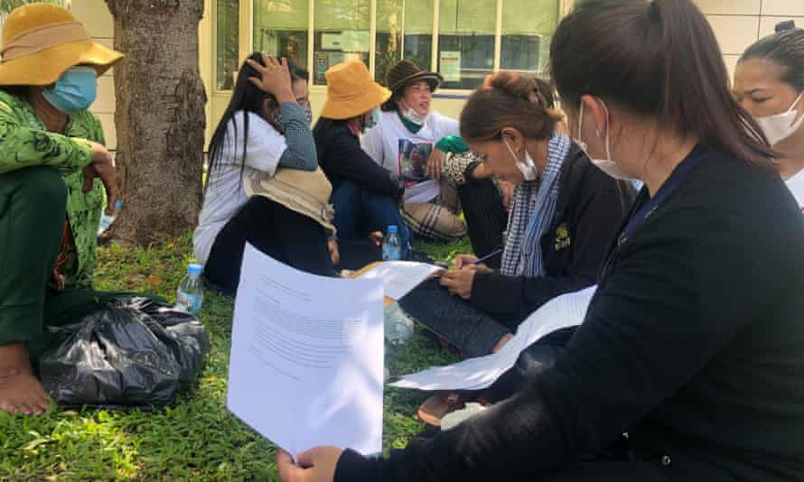 Un groupe de femmes signent un formulaire alors qu'elles sont assises sur un bord d'herbe à l'extérieur d'un bâtiment.