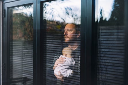 Man holding his baby daughter to his chest as he looks through the window