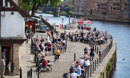People sitting at outdoor riverside tables by a city pub