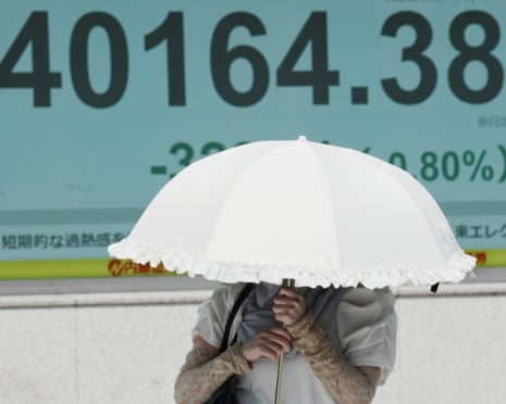 AA person walks under the intense sun near an electronic stock board displaying Japan's Nikkei index in Tokyo.