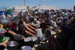 People hold pans aloft as they await food at an outdoor community kitchen