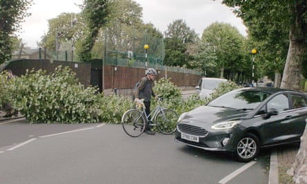 A cyclist and cars try to get around a fallen tree across the road in west London