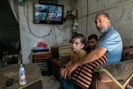 Zohar Rajabi and two of his grandchildren sit in a room with a TV on the wall