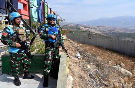 Soldiers holding rifles look towards a border wall