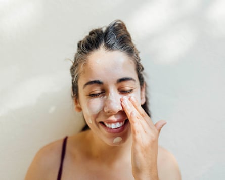 A close-up portrait of a young woman applying sunscreen to her cheeks and forehead