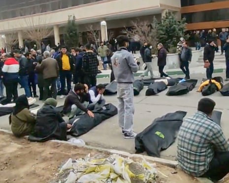 People walk between and check bodies wrapped in black sheets outside a morgue in Tehran.