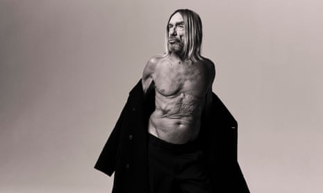 Iggy Pop naked to the waist, shrugging off a big coat